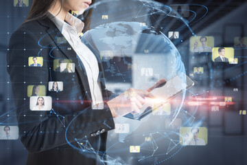 Close up of businesswoman hands using tablet with creative glowing blue globe hologram with faces on blurry office interior background. 