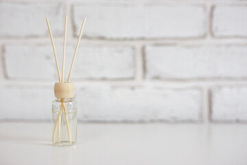 Home aroma fragrance diffuser with bamboo sticks over white brick wall background with copy space