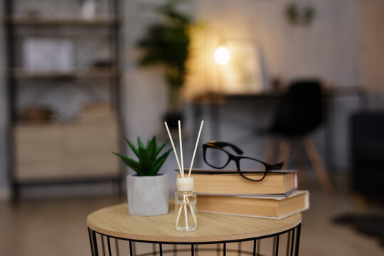 close up of reed diffuser, books, glasses and house plant on the table in living room or office