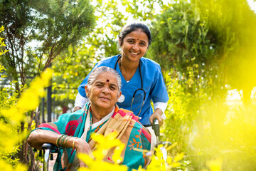 happy smiling Nurse taking senior woman on walk while on wheelchair at hospital garden by looking...