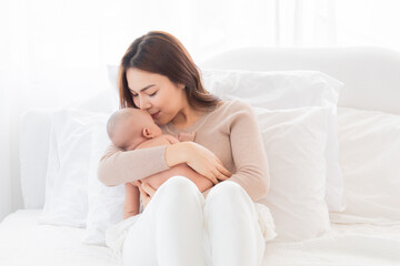 Obraz na płótnie Canvas Selective focus Beautiful Asian mother holding newborn baby and kiss baby with love and tender. Adorable infant deepy sleeping on her chest. Woman and toddler spend time together at home.
