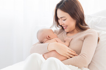 Selective focus Beautiful Asian mother holding newborn baby and looking at baby with love and showing protection. Mom and adorable infant spend time together at home.