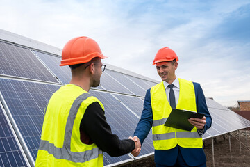 Workers in work clothes greet each other by the hand before starting work on solar panels.