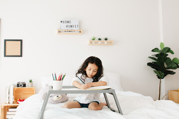 Little kid girl hands detail drawing intently with multicolored pencils in bedroom at home. on...