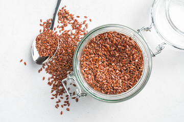 Flax seeds with a transparent jar with a spoon on a gray background. Source of omega 3, healthy food.