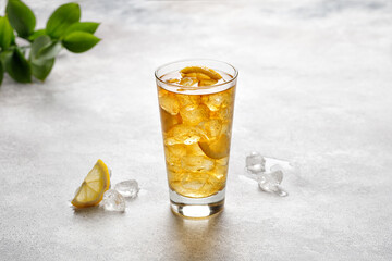 Glass of cold iced tea with ice and lemon. Lemonade with Iced Tea on grey background with green leaf