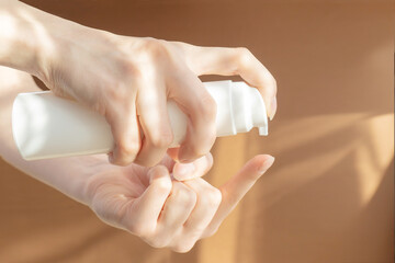 Women's hands squeeze foam for washing from bottle with dispenser onto their finger. Mockup of packaging for cosmetic products in rays of sunlight.Close-up, brown background. Concept of body care