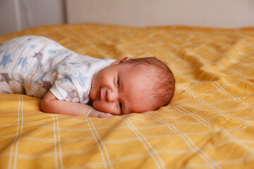 Cute bald chubby baby 2 months old lies on his stomach on yellow sheet on bed in bedroom