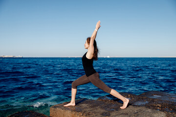 Fototapeta na wymiar Girl practices yoga on background of sea and blue sky, wind blows hair. Concept solitude of woman and nature, selfacceptance, inner harmony