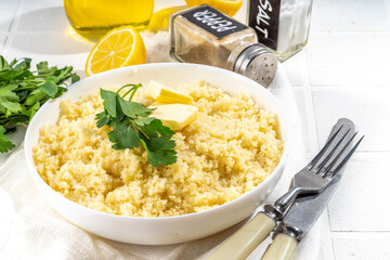 Cooked couscous with cilantro or parsley , butter, olive oil, lemon in white ceramic bowl on kitchen white table copy space