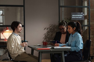Fototapeta premium Manager examining resume of young man with her colleague at table during job interview at office
