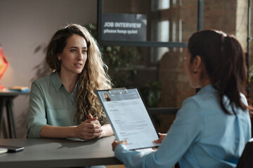 Young woman telling about her work experience while manager examining her resume at job interview