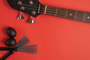 Bass guitar neck, shakers and drum brushes on a bright red background. Top view, flat lay, space for text. 