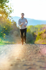 Running man jogging in rural nature at beautiful summer day. Sport fitness model caucasian ethnicity training outdoor.