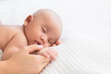 Selective focus of newborn baby deepy sleeping on white bed. Asian mother supports and holding hand adorable infant gently while toddler sleeping on bed. Child sleep in mom's hand.
