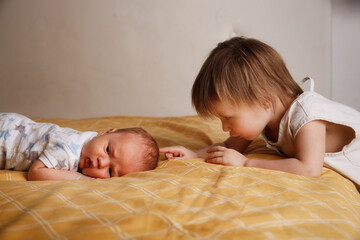 Cute bald chubby baby 2 months old and sister on bed in bedroom, baby siblings at home, toddler girl and baby in a cozy bedroom