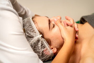 Fototapeta na wymiar Face massage. Beautiful caucasian young white woman having a facial massage with closed eyes in a spa salon