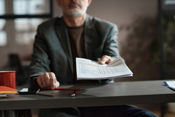 Close-up of mature businessman sitting at table and suggesting to fill the form during job interview