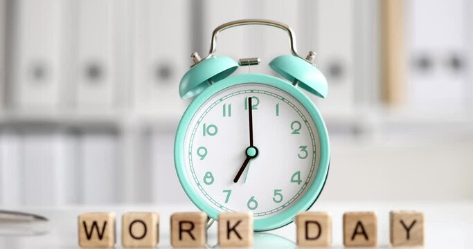 Alarm clock for seven o'clock and cubes with text working day on table in office