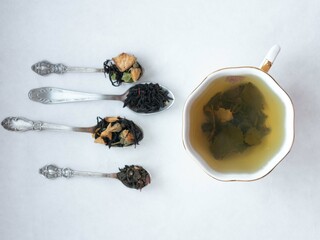 Four spoons with dry crumbly tea and a white cup on a sauvated tea sauvo on white. Tea store concept