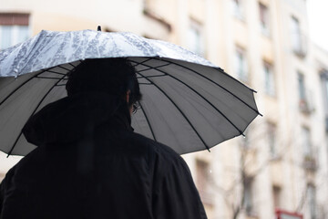 back person with black umbrella in the rain and building background