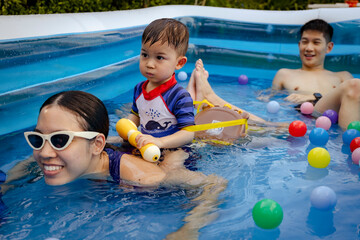 Happy Thai family playing water in the plastic pool. Lifestyle playing and having fun outdoors at summer.