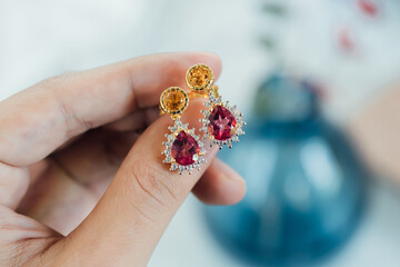 Earrings made of pink and yellow gemstones on a woman's hand.