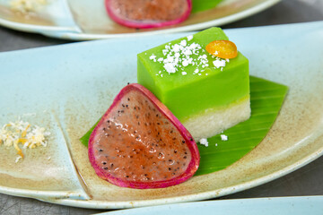 Green mochi dessert with coconut milk and slice of dragon fruit on a leave out of focus with grain