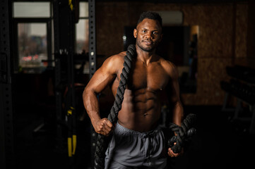Fototapeta na wymiar Muscular african american man posing with rope in gym. 