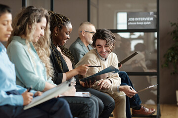 Young man smiling and discussing business contract together with woman while they sitting in waiting room and awaiting interview