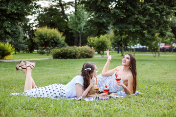 Women having picnic together, laying on the plaid on the park lawn and drinking cocktails in summer