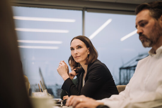 Confident mature businesswoman discussing with colleagues in office