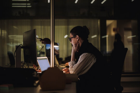 Ambitious businesswoman using laptop while working late in office at night