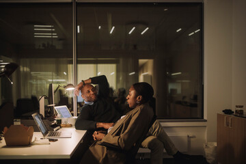 Businesswoman talking with male colleague sitting at work place