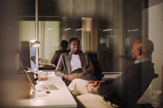 Smiling businesswoman planning strategy with male colleague seen through glass of work place