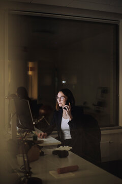 Mature businesswoman talking on smart phone while working late in office