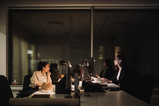 Businesswoman talking with female colleague while working overtime at work place