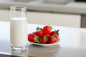 Glass of milk and plate with pile of fresh strawberries set on the table.