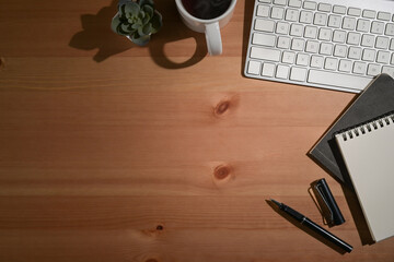 Simple workplace with wireless keyboard, notebook and coffee cup on wooden table. Top view.