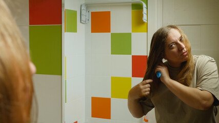 A girl standing in the bathroom against the mirror brushing her long, wet hair. There are colorful...
