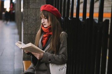 Beautiful Caucasian woman wearing coat, beret, scarf and bag with text (happiness) sitting alone on Saint Petersburg metro station reading a book. Image with selective focus and noise effect