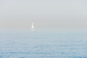 Fototapeta premium Seascape. Haze over the blue surface of the sea. Yacht on a background of calm sea and blurred horizon.