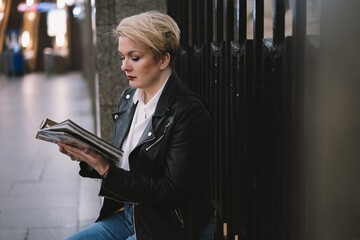 Caucasian short haired woman wearing leather jacket sitting alone on Saint Petersburg metro station reading a book. Image with selective focus and noise effect