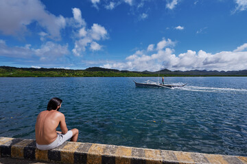 Young man sitting on wooden fishing pier with beautiful tropical sea view.