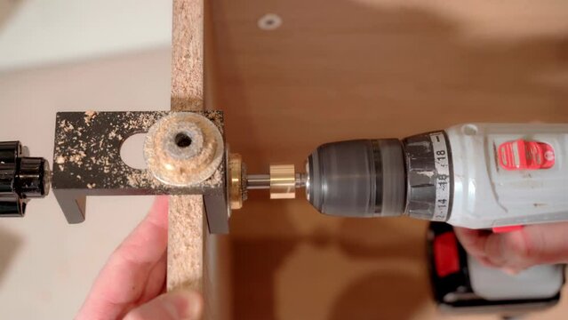 The master uses a jig template and an electric screwdriver to drill holes when assembling the cabinet.