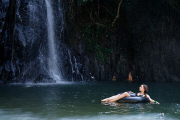Fototapeta na wymiar Travel and nature. Young woman swimming in tropical waterfall pool.