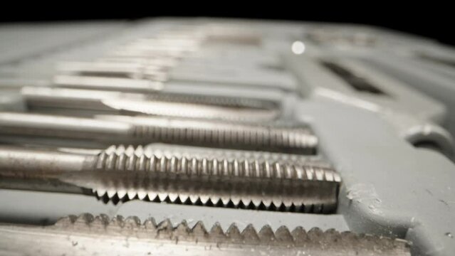 A set of taps for cutting threads in metal in a box. Dolly slider extreme close-up. Laowa Probe