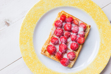 Warm Belgian waffle with fresh strawberries and suger on a plate with copy space