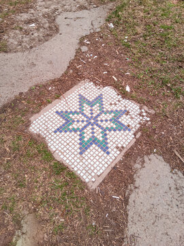 Decorative slab with a mosaic of a ruined house lies on the ground.