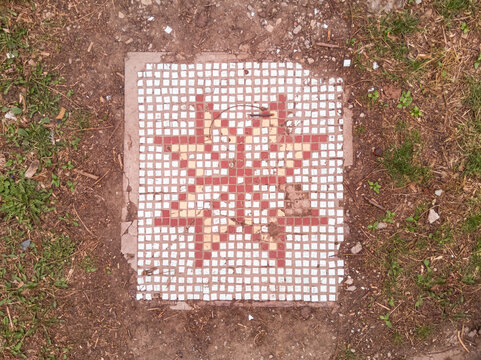Decorative slab with a mosaic of a ruined house lies on the ground.